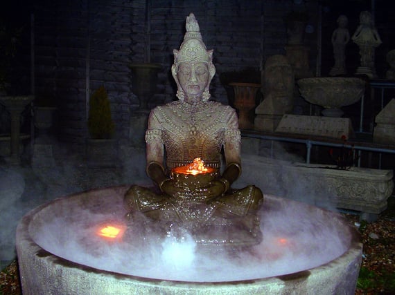 Serene Buddha stone fountain running with water and a lit bowl at dusk