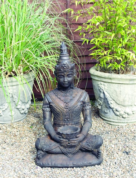 Serene Buddha stone fountain in umber finish on gravel beside garden planters