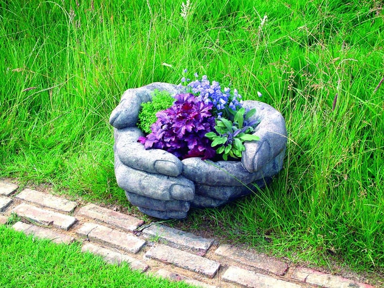 Cupped Hands stone planter holding herbs in a UK garden